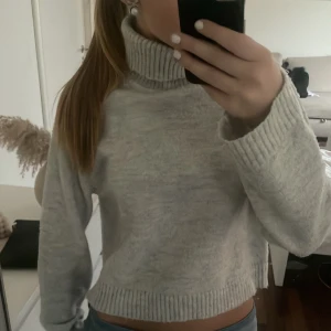 Grå stickad polotröja från Gina Tricot - Säljer en mysig grå stickad polotröja från Gina Tricot. Tröjan har en hög polokrage och långa ärmar med ribbade muddar. Perfekt för kyliga dagar! 