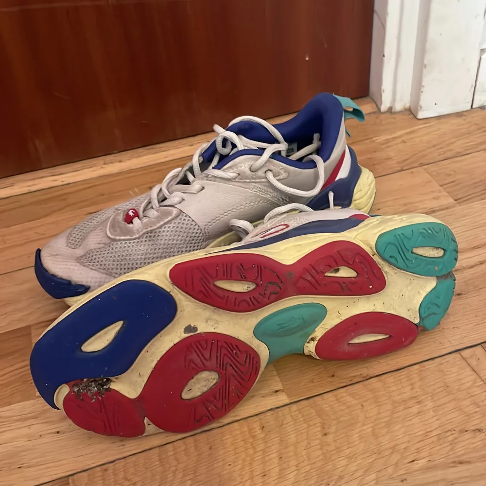 Säljer ett par unika sneakers från Lacoste med en färgglad design. Skorna har en vit bas med inslag av blått, rött och grönt. De har snörning och en rund tå, samt en mönstrad sula i flera färger. Perfekta för dig som vill sticka ut!. Kengät.