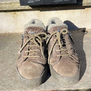 Bruna sneakers med foder och dragkedja - Säljer ett par bruna sneakers från Giuseppe Zanotti med mjukt foder och dragkedja på sidan. Skorna har snörning och en rund tå, vilket ger en bekväm passform. Perfekta för kyligare dagar.