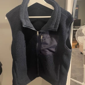 Mörkblå fleeceväst med dragkedja - Säljer en mörkblå fleeceväst med dragkedja och en praktisk bröstficka. Perfekt för lite skönare dagar och ger en mysig känsla. Passar perfekt med huddie under. Storlek m