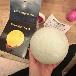 Moon Night Light led lampa  - Säljer en Moon Night Light som ser ut som en måne. Den kommer med en fjärrkontroll för att ändra färger och en träställning. Perfekt för att skapa en mysig atmosfär i rummet. Inkluderar även en USB-kabel för laddning. 10cm  mån lampa 