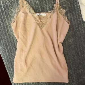 Beige/Rosa linne från NA-KD - Säljer en stilren topp från NA-KD med spetsdetaljer. Toppen har tunna axelband och en v-ringad design. Aldrig använd faktiskt
