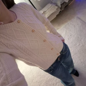 Vit stickad kofta från H&M - Säljer en mysig vit stickad kofta från H&M med ett klassiskt flätmönster. Koftan har långa ärmar och knäpps med dekorativa knappar framtill. Perfekt för kyliga dagar!🤍 skriv vid intresse!💕