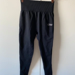 Svarta leggings från ICIW - Snygga svarta leggings från ICIW med hög ribbad midja för extra komfort. Perfekta för träning eller en avslappnad dag. Diskret logga på benet ger en stilren look.🩷