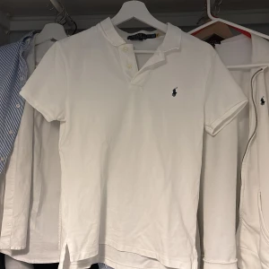 Vit kortärmad pikétröja från Ralph Lauren - Säljer en klassisk vit kortärmad pikétröja från Ralph Lauren. Tröjan har en broderad logotyp på bröstet och knappar vid kragen. Perfekt för en stilren look.