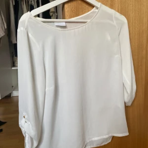 Vit blus - Säljer en vit blus från Vila med knappar längs ryggen. Blusen har trekvartsärmar med knappdetalj och en rund halsringning.💘