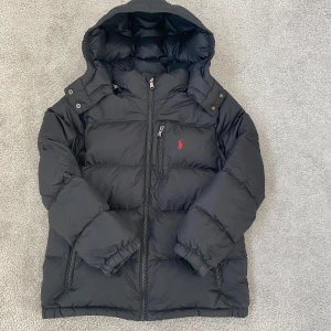 Svart Ralph Lauren jacka  - Svart Ralph Lauren vinterjacka för barn i storlek M(10-12 år. Allt funkar som de ska förutom att hängöglorna har tyvärr gått sönder men annars är den i bra skick och fungerar som den ska 👍