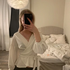Vit omlottblus - Säljer en elegant vit omlottblus med trekvarts ärmar och knytband i midjan. Perfekt för en stilren look. 💫