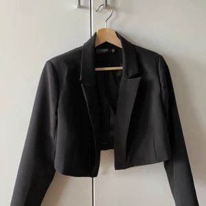 Svart kavaj från Missguided - Snygg svart kavaj från Missguided i petite-storlek. Kavajen har en croppad design med långa ärmar och en klassisk krage. Perfekt för en stilren look.
