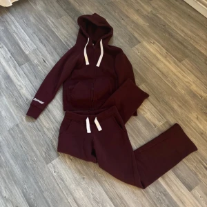 Vinröd hoodie från Russedress XS - Mysig vinröd hoodie från Russedress i storlek XS. Tröjan har huva med vita snören, dragkedja framtill och fickor. Ärmen har tryckt logga och materialet är mjuk bomull, perfekt för chill dagar. Även matchade mjukis byxor till🥰