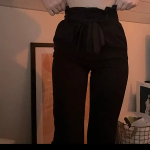 Svarta kostymbyxor med knytning - Säljer ett par svarta högmidjade kostymbyxor med knyt i midjan. Byxorna har raka ben. För korta i benen på mig