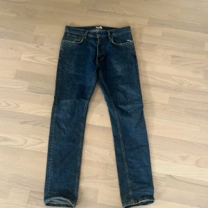 Taktíl William Tapered jeans blå - Mörkblå jeans från Taktíl, modell William Tapered. Klassisk femficksdesign med snygga kontrastsömmar och vit patch bak i midjan. Jeansen har en tapered passform som smalnar av nedtill och är tillverkade i slitstarkt denimtyg.