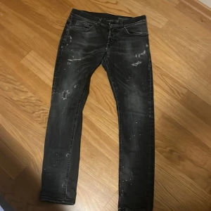 Svarta  jeans från Dondup George - Säljer ett par svarta skinny jeans från Dondup, modell George. Jeansen har slitna detaljer, små hål och färgstänk för en riktigt edgy look. Klassisk femficksmodell med låg midja och smal passform. Perfekta för dig som gillar streetstyle, pris kan diskuteras vid snabb affär!