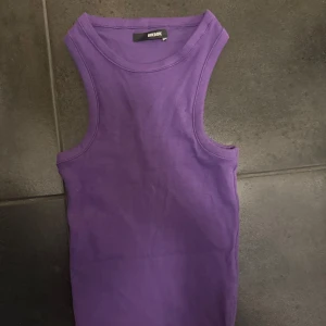 Lila ribbad linnetopp från Bik Bok - Snygg lila ribbad linnetopp från Bik Bok med klassisk rund halsringning och ärmlös design. Perfekt att styla med jeans eller kjol för en cool och enkel look. Toppens material är mjukt och stretchigt för extra komfort.