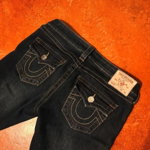 True Religion jeans - Säljer ett par mörkblå jeans från True Religion med ikoniska bakfickor och kontrastsömmar. Klassisk femficksmodell med snygga detaljer och grova sömmar. Jeansen är även skräddarsydda till L 31/32 och W 27. 