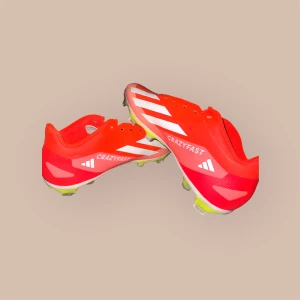 Adidas Crazyfast röda fotbollsskor - Snygga Adidas Crazyfast fotbollsskor i röd färg med vita detaljer och klassiska tre ränder på sidan. Skorna har låg profil, platt sula med dobbar och är tillverkade i syntetmaterial. Perfekta för dig som vill sticka ut på planen.