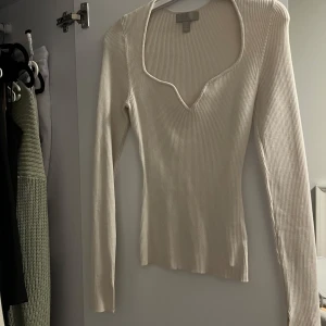 Ribbad långärmad topp - Säljer en ribbad beige långärmad topp med djup v-ringning och slits vid armen. Toppen är tillverkad i ett stretchigt material. Den har använts 3-4 ggr. 