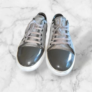 Grå Captoes skor från Lanvin - Snygga grå sneakers från Lanvin med cool lackad tå i mörkgrått och ovandel i mocka. Skorna har vita sulor, grå snörning och diskreta metalldetaljer vid snörhålen. Perfekta för dig som gillar en stilren men ändå unik look. Riktigt schyssta inför hösten och vintern. Modellen är captoe och det finns inga repor på själva captoen. Sulan har lite slitage (om video frågas så be om det så skickar jag) storleken är uk9 alltså 43/44