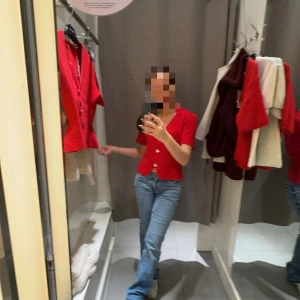 Röd kortärmad topp från Gina Tricot - Superfin röd topp från Gina Tricot med v-ringning och snygga knappar framtill. Modellen är lite croppad och har korta ärmar. Perfekt att styla med jeans eller kjol för en cool look. Materialet känns mjukt och har en lätt stretch.