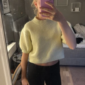 Ljusgul stickad croppad tröja - Superfin ljusgul stickad tröja med croppad passform och puffiga korta ärmar. Tröjan har ribbad halsringning och nederkant, perfekt för lager på lager eller som statement-piece till jeans eller kjol.