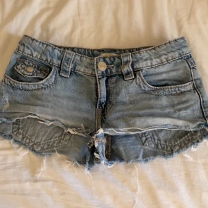 Blå lågmidjade jeansshorts med broderade fickor💕 - Snygga ljusblå jeansshorts från Gina Tricot med fransig kant och broderade bakfickor. Klassisk femficksmodell, låg midja och slitna detaljer för en cool vibe. Perfekta för sommaren och festivalhäng! Dom är ifrån Gina Young 💝💝