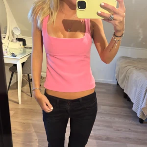 Rosa linnetopp med breda axelband - Säljer en snygg rosa linnetopp med breda axelband och fyrkantig urringning. Toppen är croppad och har en stilren, enkel design som passar perfekt till jeans eller kjol. Materialet känns mjukt och följsamt mot kroppen. Perfekt för dig som gillar färg och vill sticka ut.