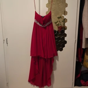 Röd långklänning med pärldetaljer - Säljer en röd långklänning från WISCO med tunna axelband och vacker pärldekor under bysten. Klänningen har ett flowigt lager på lager-utseende och asymmetrisk nederkant. Perfekt för dig som vill sticka ut med en elegant och färgstark look.