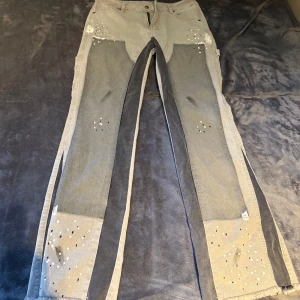 Denim byxor - Unika gråa cargopants med pärldetaljer på fickor och benslut. Byxorna har breda slitsar längs benen och coola kontrastpaneler i mörkare grått framtill. Raka ben och flera fickor ger en avslappnad vibe. Perfekta för dig som vill sticka ut med din stil.