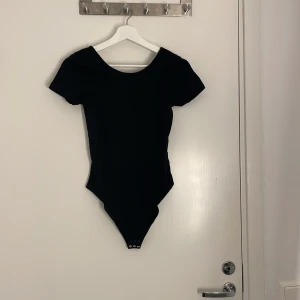 Svart kortärmad bodysuit - En svart, enkel och stilren bodysuit med korta ärmar och rundad halsringning. Bodyn har knäppning nedtill och är figurnära i modellen, perfekt att styla med jeans eller kjol för en clean look.