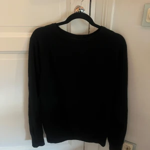 Svart stickad tröja med rund hals - En enkel mörkblå stickad tröja med rund hals och långa ärmar. Perfekt för att bygga lager på hösten eller vintern. Tröjan har en klassisk passform och är mjuk mot huden, vilket gör den skön att bära hela dagen.