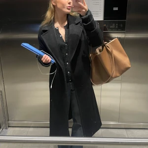 Svart lång kappa från zara - Säljer en svart lång kappa med breda slag och dubbelknäppning. Snygg och tidlös modell med rak passform och diskreta fickor. Perfekt för dig som vill ha en stilren look under höst och vinter. Passar till allt och ger en clean vibe.