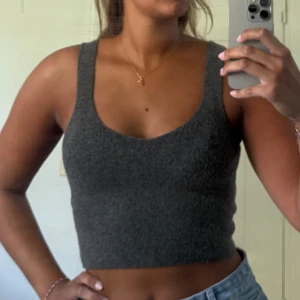 Ull linne - Säljer en mörkgrå croppad topp från Zara med breda axelband och rundad urringning. Toppen är stickad och har en tight passform som sitter snyggt till både jeans och kjol. 