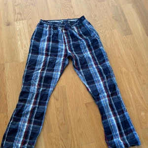 Rutig pyjamasbyxor från Gant, storlek L - Säljer ett par sköna pyjamasbyxor från Gant i storlek L. Byxorna har ett rutigt mönster i blått, rött, vitt och svart med elastisk midja och Gant-logga på linningen. Perfekta för chill hemma eller när du vill vara extra bekväm. Köpt för 749kr mitt pris 379kr.