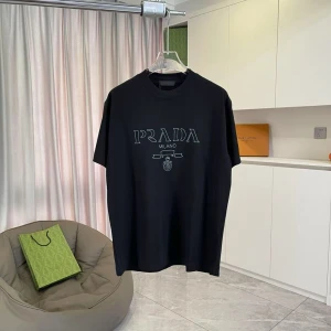 Svart t-shirt från Prada Milano - Svart t-shirt från Prada Milano med stilren logotyp i ljusblått broderi på bröstet. Klassisk rund hals och korta ärmar. T-shirten är gjord i mjuk bomull och har en clean, oversized vibe som passar perfekt till streetwear. Snygg att matcha med jeans eller shorts.