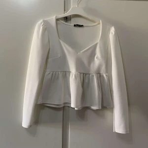 Vit blus med v-ringning från Missay - Supersöt vit blus från Missay med v-ringad hals och långa ärmar. Toppen har en volang nedtill som ger en flowy och feminin look. Perfekt att styla med jeans eller kjol för en trendig outfit.