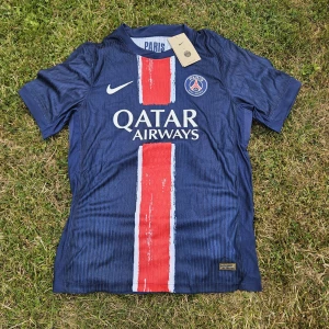 PSG Neymar 10 matchtröja Nike blå - Paris Saint-Germain fotbollströja med Neymar 10 på ryggen. Tröjan är marinblå med en röd vertikal rand och vita detaljer. Tillverkad i lätt Dri-FIT ADV-material som andas. Klassisk passform med korta ärmar och klubbmärke på bröstet.