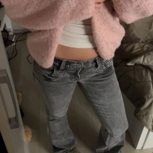 Grå bootcut jeans med låg midja - Säljer ett par grå tvättade jeans med bootcut-modell och låg midja. Jeansen har klassisk femficksdesign, bälteshällor och stängs med knapp och dragkedja. Materialet är jeans och färgen är en snygg tvättad grå som ger en cool vibe.