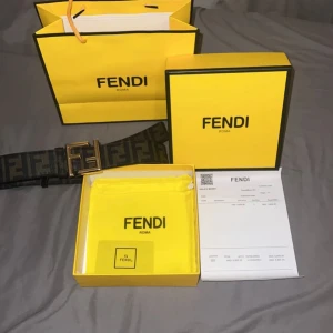 Svart Fendi bälte med FF-logga - Säljer ett svart bälte från Fendi med klassiskt FF-mönster och stor guldfärgad Fendi-logga som spänne. Bältet är gjort i skinn och har en lyxig känsla, perfekt för att lyfta vilken outfit som helst. Kommer med originalförpackning och dustbag.