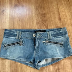 Blå jeansshorts med dragkedjor - Snygga blå jeansshorts med låg midja och coola detaljer som dragkedjor på framfickorna. Snygga slitna effekter. 