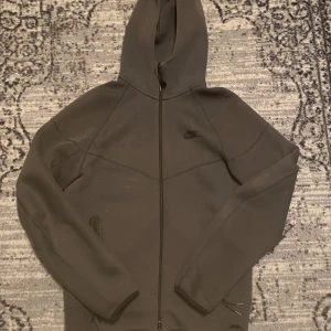 Nike tech hoodie  - Snabb leverans! Nike tech som är i fantastisk skick! Säljer en svart hoodie från Nike i storlek S. Tröjan har hel dragkedja, två fickor med dragkedja och en klassisk huva. Materialet är mjukt och tjockt, perfekt för kyliga dagar. Snygg och stilren design med diskret Nike-logga på bröstet.