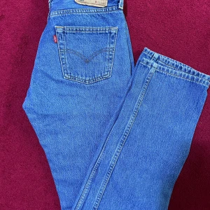 Levi's 501 blå jeans W30 L34 - Klassiska Levi's 501 jeans i ljusblå denim med raka ben och hög midja. Byxorna har fem fickor, knappgylf och den ikoniska läderpatchen bak. Perfekta för dig som gillar en tidlös och avslappnad look.