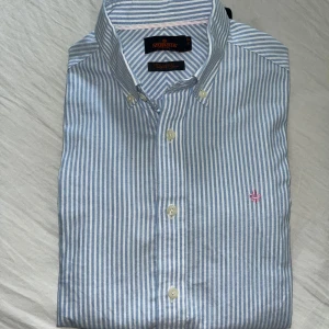Randig skjorta från Morris Stockholm - Snygg skjorta från Morris Stockholm i blåvitt randigt mönster. Klassisk button-down krage, vita knappar och broderad rosa logga på bröstet. Tillverkad i mjuk bomull och har lång ärm. Perfekt för en clean och stilren look. Storlek 38/S-M Tveka inte att fråga om ni vill ha fler bilder eller undrar något, Mvh Olle.
