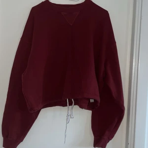 Vinröd croppad sweatshirt med snörning - Säljer en vinröd croppad sweatshirt med långa ärmar och snörning i nederkanten. Tröjan har en relaxed passform och är perfekt för dig som gillar en chill och trendig stil. Mjuk bomullskänsla och enkel att matcha med jeans eller leggings.