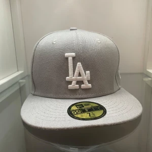 Grå LA New Era  - Snygg grå LA Dodgers keps från New Era 59FIFTY-serien. Kepsen har broderad LA-logga framtill. Rak skärm och klassisk passform. Tillverkad i polyester för en clean och modern look. Vet ej om den är äkta.