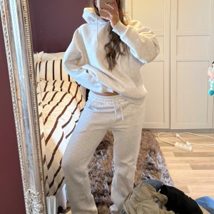 LXA mjukisset - Säljer en ljusgrått mjukisset från LXA med grönt tryck på ryggen. Hoodie har huva med snörning och en relaxed, oversized passform. Hoodien är i syorlek M och mjukisbyxorna storlek S.