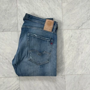 Replay Waitom jeans blå, stl 32 - Snygga Replay Waitom jeans i klassisk blå tvätt med lätt slitna detaljer och raka ben. Jeansen har fem fickor, knappgylf och diskret Replay-logga vid fickan. Perfekta för dig som gillar en avslappnad men stilren look.