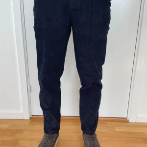 Mörkblå manchesterbyxor Tommy Hilfiger - Snygga mörkblå manchesterbyxor från Tommy Hilfiger. Byxorna har raka ben, normal passform och klassiska fickor både fram och bak. Materialet är mjukt och skönt manchester. Tveka inte att kontakta vid frågor.