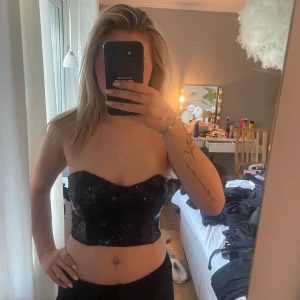 Svart paljettkorsett från Bik Bok - Säljer en svart glittrig korsett från Bik Bok i storlek S. Toppen är axelbandslös och täckt med paljetter, har en croppad passform och stängs med hyskor i ryggen. Perfekt för att sticka ut och ge outfiten extra edge.