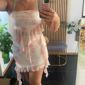 Rosa och vit kortsett med volanger - Supersöt kort sett i rosa och vitt med volangdetaljer. Klänningen har ett mjukt, molnigt mönster. Väldigt fin och skönt och använt 1-3 gånger🤍