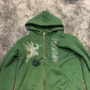 Grön hoodie från Laviago - Säljer en grön hoodie från Laviago med dragkedja och en cool design på framsidan. Hoodien har en stor ficka framtill och en justerbar huva. Perfekt för en avslappnad stil.